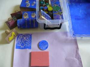 Selbstgebastelte Model aus Holz, Gummi und Nägeln offen und in einer Kisten. Davor ein Beispieldruck von einem Pfau.