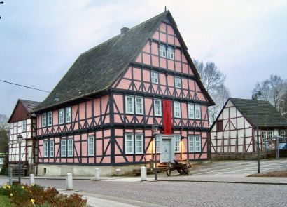 Ein vierstöckiger Fachwerkbau mit Sandsteindach, umgeben von kleineren Nebengebäuden
