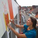 Eine Frau bemalt eine Hauswand mithilfe von Schablonen