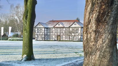 Museum Seesen,  Ansicht des Fachwerkgebäudes vom Park aus durch ein paar Bäume gesehen. Ein klarer Winterhimmel steht über dem Gebäude und Frost bedeckt die Wiese davor. Foto Wikimedia Commons
