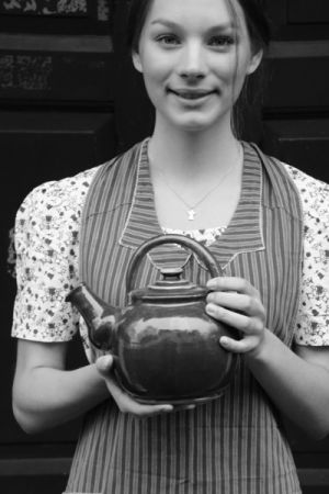 Schwarz-weiß Aufnahme einer jungen Frau mit einer großen Teekanne in der Hand.