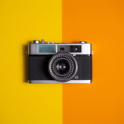 Retro-Konica-Kamera auf einer leuchtend gelben und orangefarbenen Oberfläche