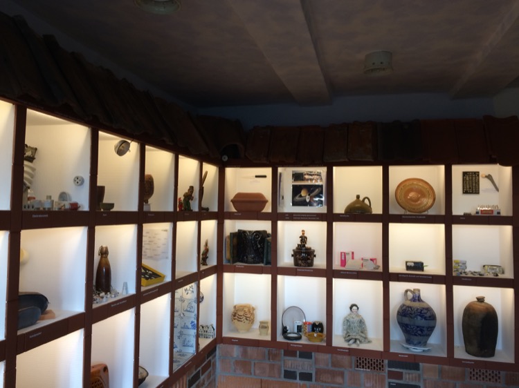 In einem gemauert Regal mit hell erleuchteten quadratischen Fächern stehen unterschiedliche Gegenstände aus Keramik
